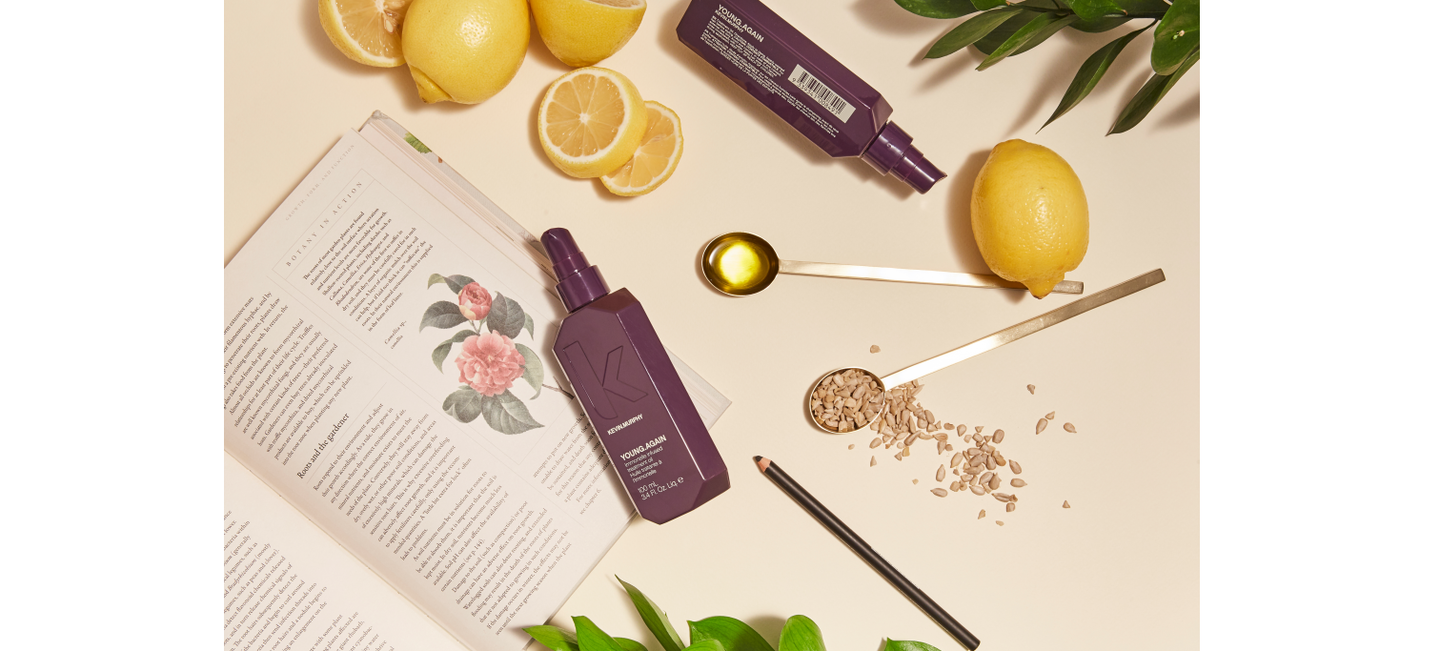 "Aesthetic composition of KEVIN.MURPHY YOUNG.AGAIN bottles, sliced lemons, metallic spoons, and green foliage on a cream surface."